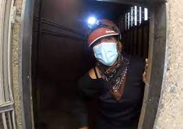 Person with headlamp and mask walking through tunnel.