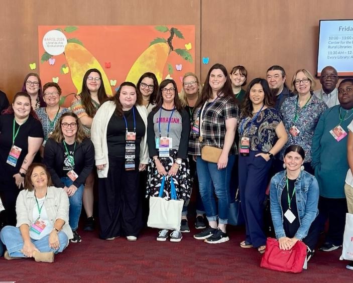 Group of smiling ARSL conference attendees in front of an ARSL 2024 banner.