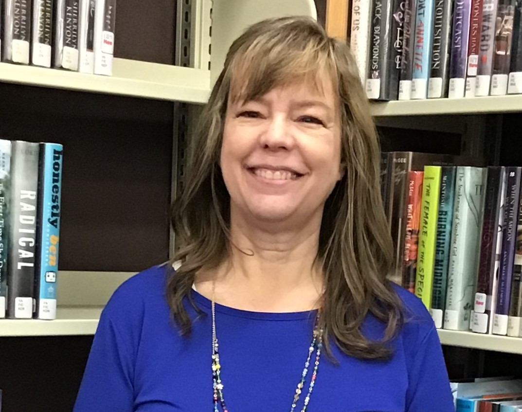Joyce Baker smiling in front of library shelves.