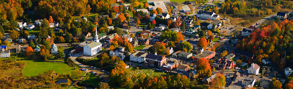 Aerial shot of small town with steeple surrounded by trees in Autumn.